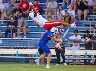 Football player in blue tackles player in white and red mid-air.