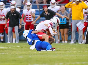 A football player in blue tackles an opponent in white during a game.