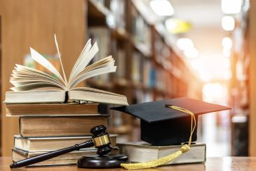 Graduation cap, gavel, and books on a table in a library.