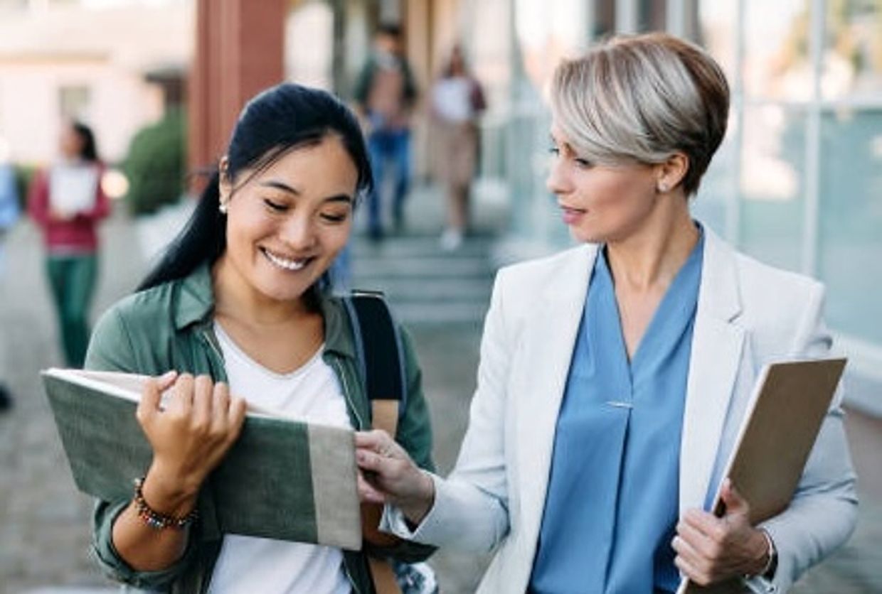 Two women discussing a document outdoors, one smiling and the other pointing.
