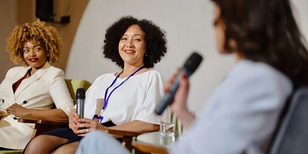 Three women engaged in a discussion, holding microphones in a professional setting.