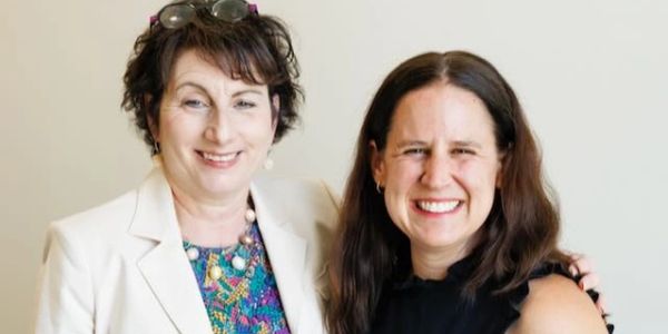 Two women smiling together in a friendly pose indoors.