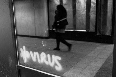 Black and white photo showing graffiti that says 'virus' and a blurred figure walking.