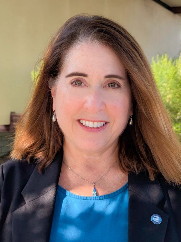 Smiling woman with brown hair wearing a blue blouse and black blazer.