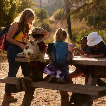 Kids gathered around a picnic table outdoors.