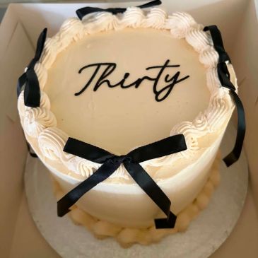 Elegant cake with 'Thirty' written and black ribbons.