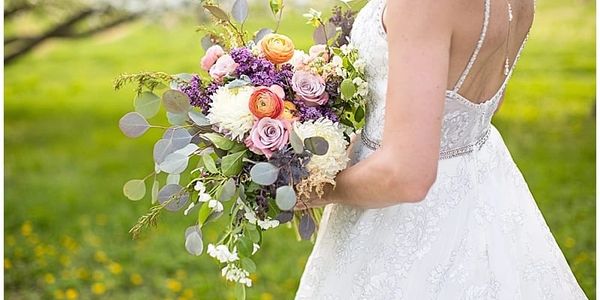 Bride in white dress holding a colorful floral bouquet outdoors.