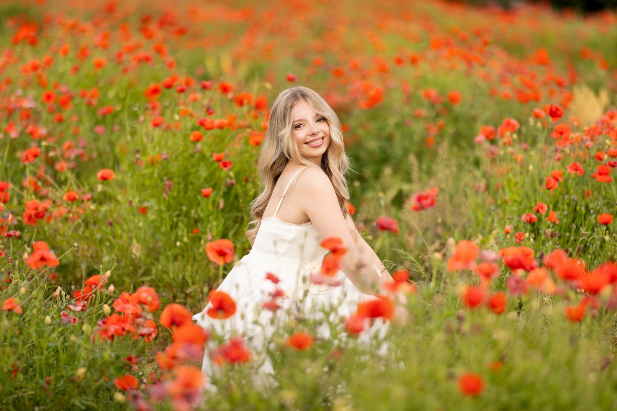 Smiling young woman in white dress in a field of red flowers.