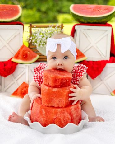 Baby biting into a watermelon cake.