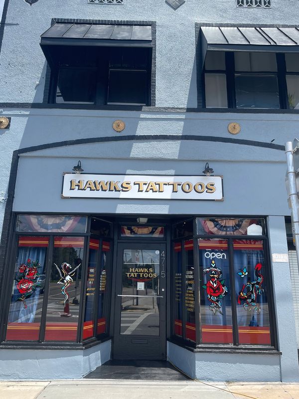 Front view of Hawks Tattoos shop with colorful window art and signage.