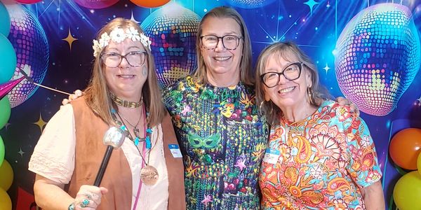 Three women smiling at a party with colorful disco decorations.