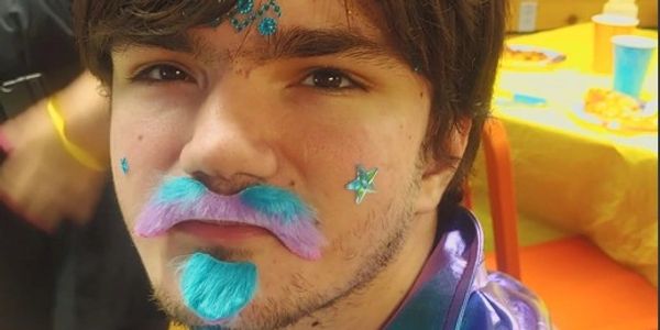 Young man with colorful face paint and blue-purple mustache and beard.