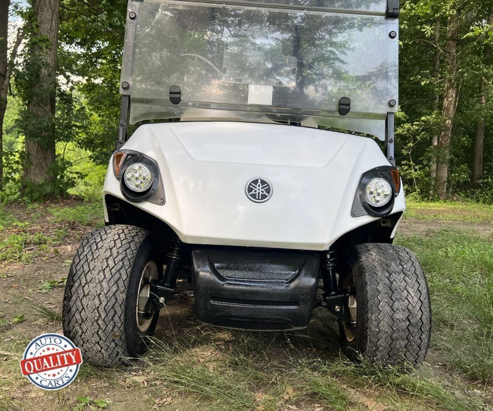 Front view of a white Yamaha golf cart in a forest setting.