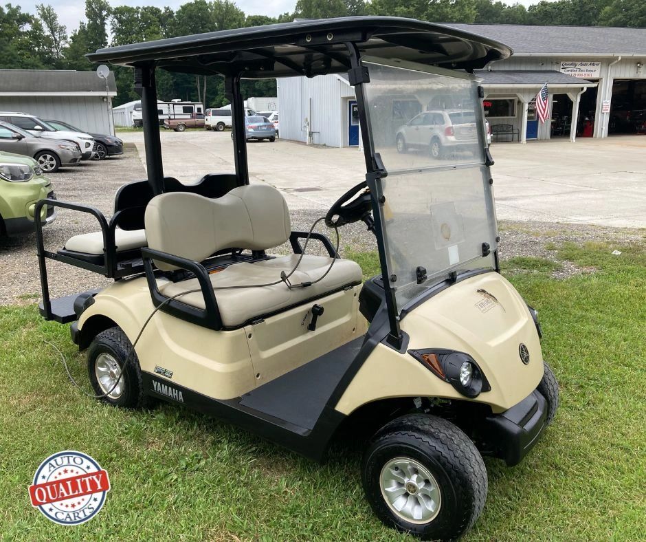 Beige Yamaha golf cart with roof parked on grass.