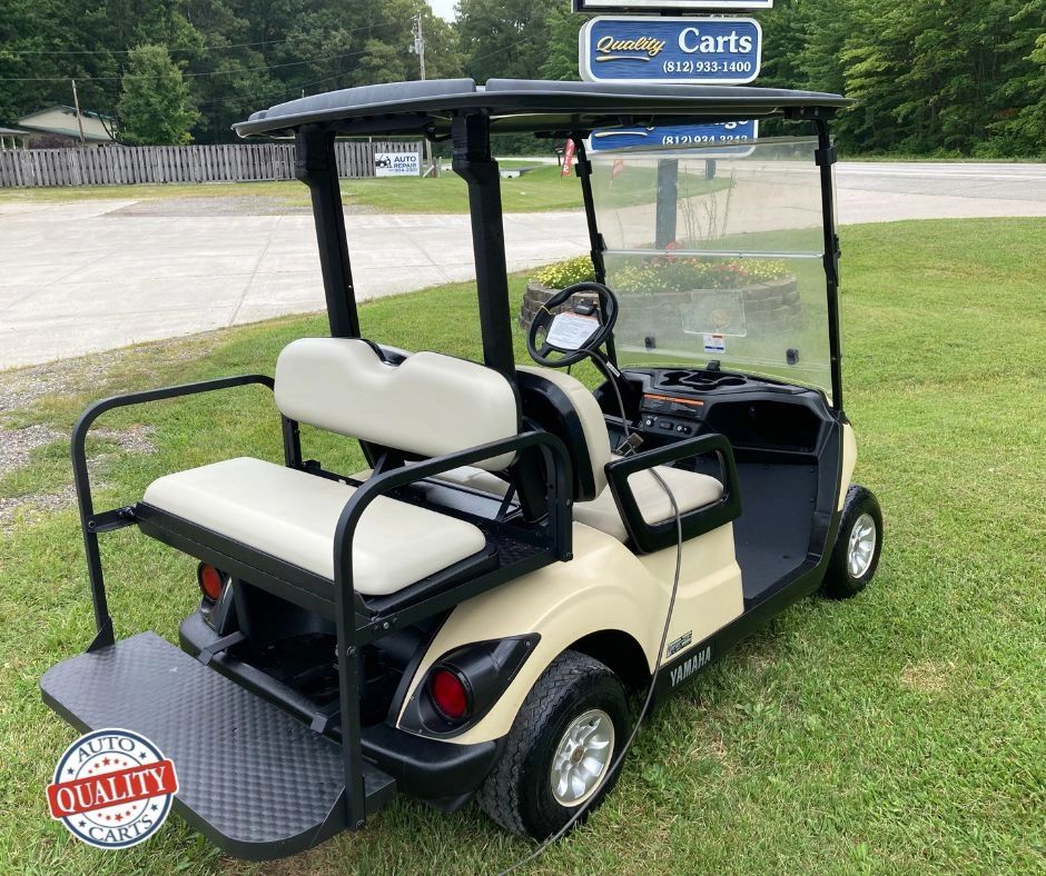 Beige Yamaha golf cart with rear seating on grass.
