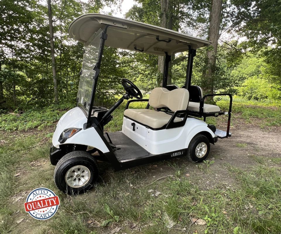 White Yamaha golf cart parked on grass near trees.