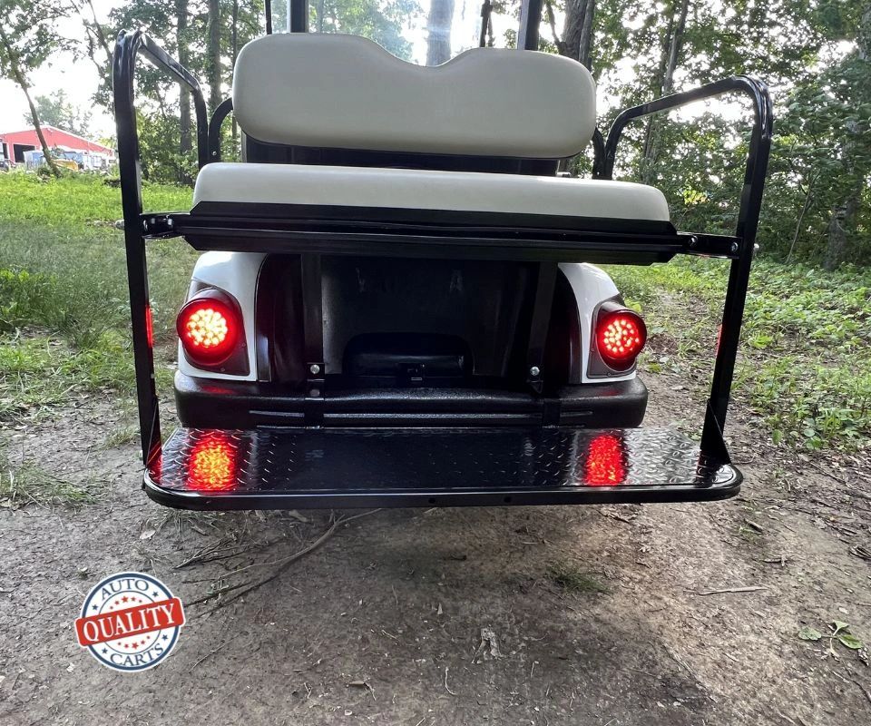 Rear view of a golf cart with illuminated red brake lights in a wooded area.