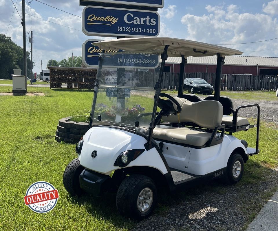 White Yamaha golf cart parked on grass near Quality Carts signs.