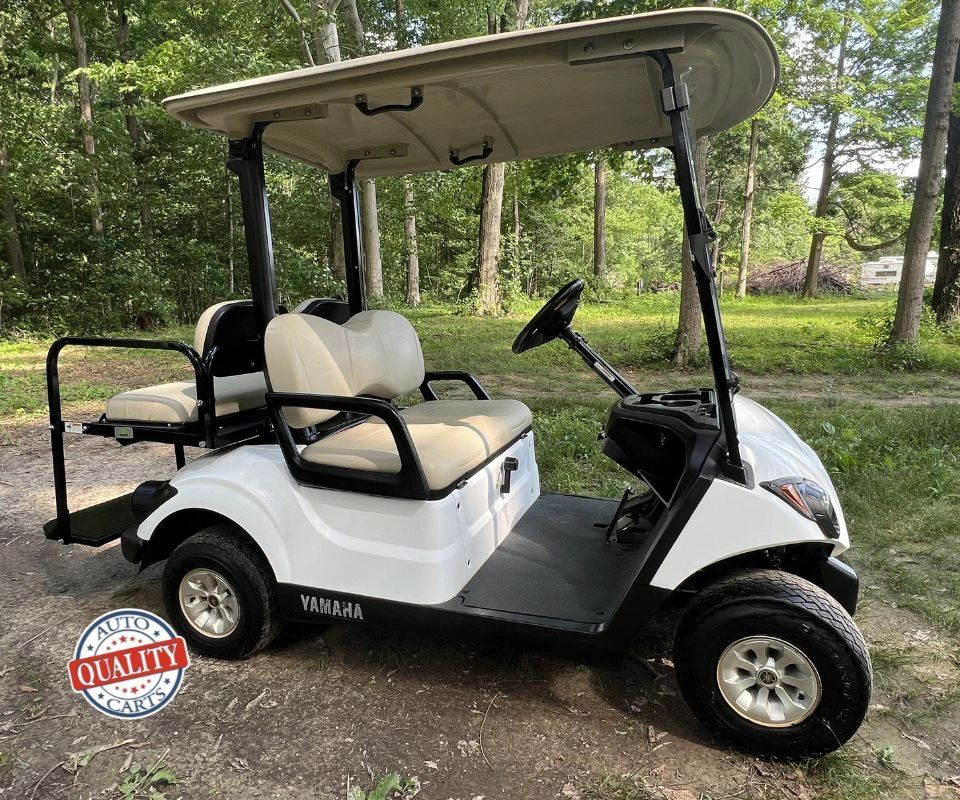 White Yamaha golf cart parked on a dirt path surrounded by trees.