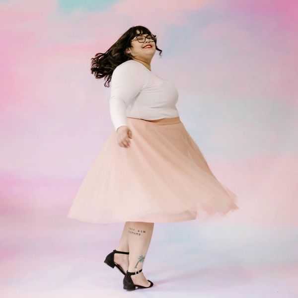 Woman joyfully twirling in a pink skirt against a pastel sky background.