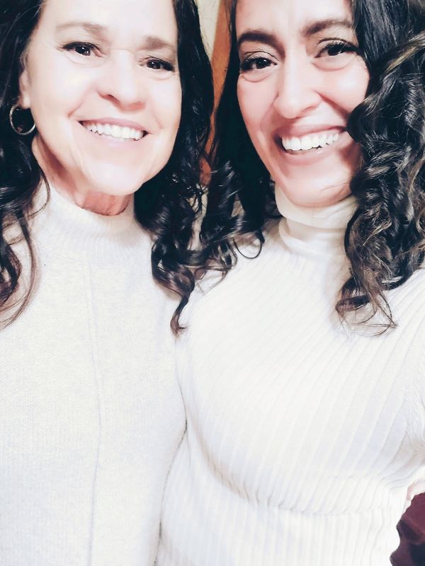 mother and daughter with dark curling hair, smiling, in white dressy shirts