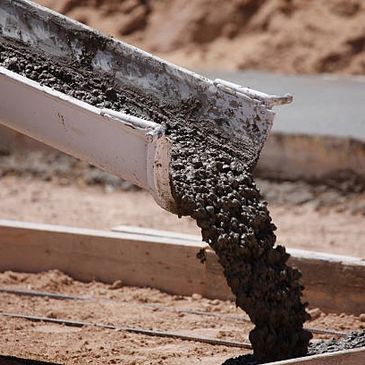 Wet concrete pouring out of a concrete truck chute into concrete forms.