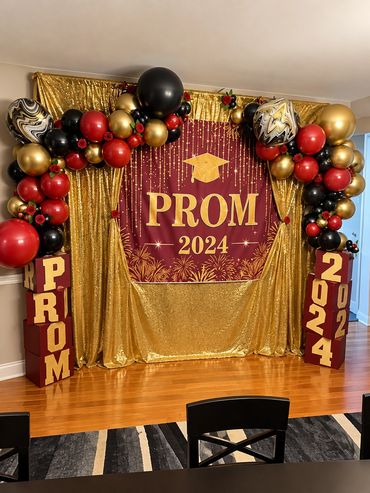 Prom 2024 backdrop with red, black and gold balloon garland and gold sequin curtains.