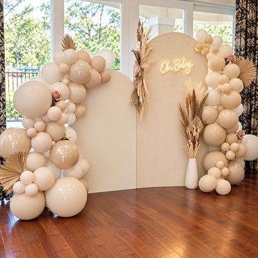 Elegant neutral-toned baby shower backdrop with a beige and cream balloon arch framing a white panel
