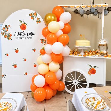 Citrus-themed baby shower dessert display with an orange and white balloon column, an 'A Little Cuti