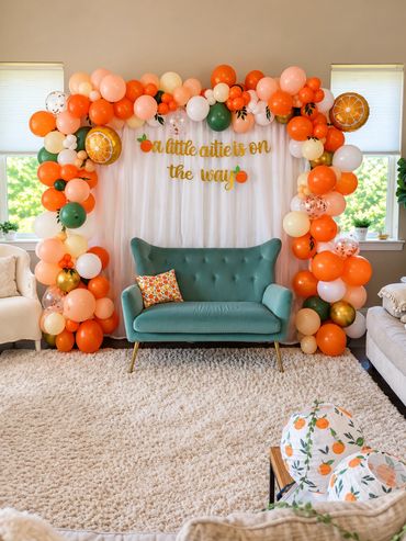 Orange-themed baby shower backdrop with a lush orange, peach and cream balloon arch framing white cu