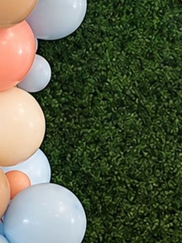 Pastel balloon garland in peach, pink, blue and cream cascading along the edge of a lush green grass