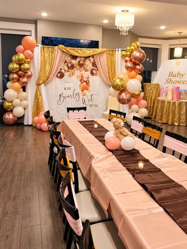 Pink and gold birthday party room with a long dining table dressed in a pink tablecloth and brown ru