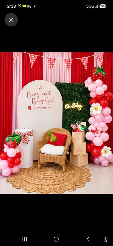 Strawberry-themed birthday party setup with red and pink balloon columns flanking red draped curtain