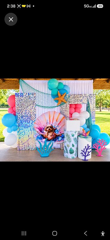 Under-the-sea birthday backdrop with a blue sequin wall, fishing net, starfish and seashell decor. B