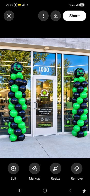 Grand opening balloon columns in green and black flanking the glass entrance doors of a storefront. 