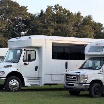 Two white shuttle buses parked on grass.