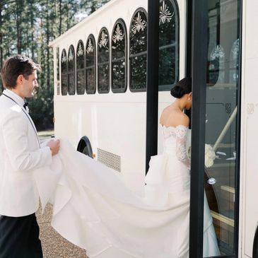 Groom holding bride's train as she boards a bus.
