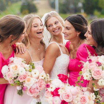 Bride with bridesmaids holding bouquets, all smiling joyfully.
