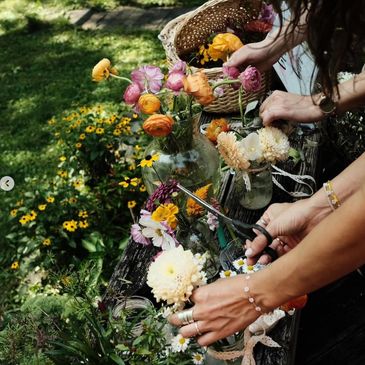 Hands arranging vibrant flowers in glass vases outdoors.