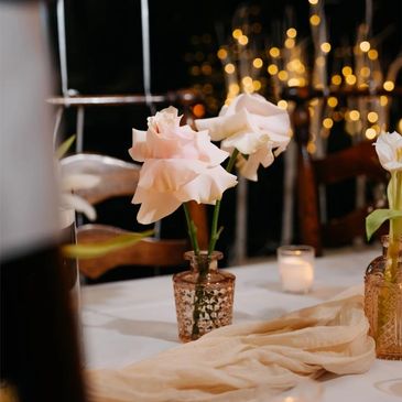 Soft pink roses in a rustic vase on a decorated table with warm lights.