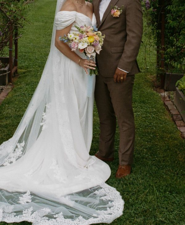 Bride and groom in wedding attire holding bouquet outdoors.