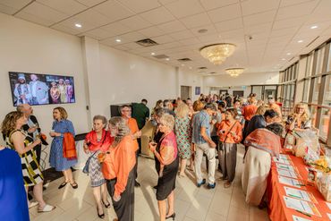 People mingling at a social event in a well-lit room with large windows.
