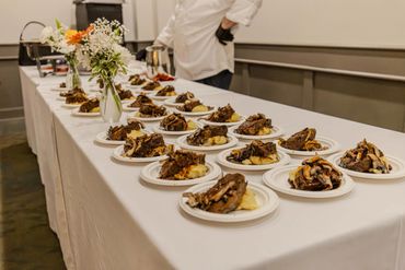 Multiple plates of gourmet food lined up on a banquet table with a chef in the background.