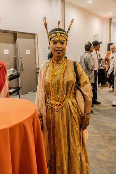 Woman in traditional golden attire and ornate headpiece at an indoor event.