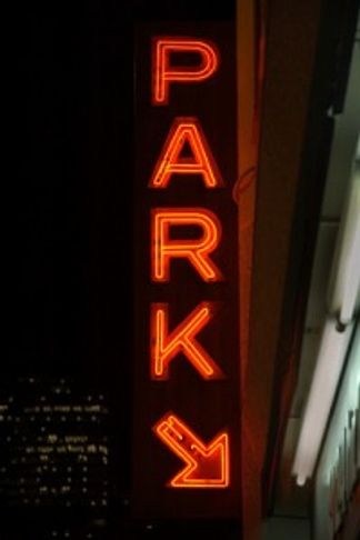 Neon red sign reading 'PARK' with an arrow pointing down and right at night.