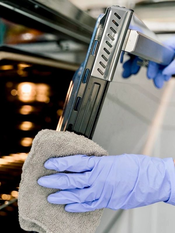 Cleaning an oven rack with a cloth and wearing gloves.