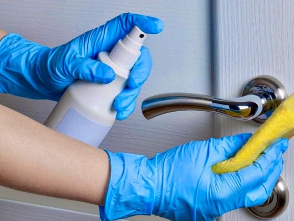 Person disinfecting door handle with gloves and spray.