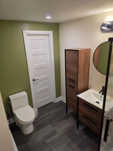 Salle de bain moderne avec mur vert et meuble en bois.