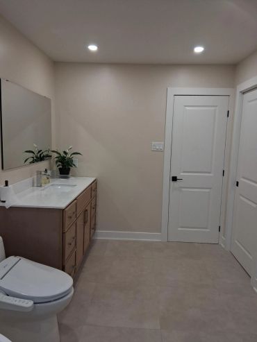 Salle de bain moderne avec meuble-lavabo, toilettes et portes blanches.