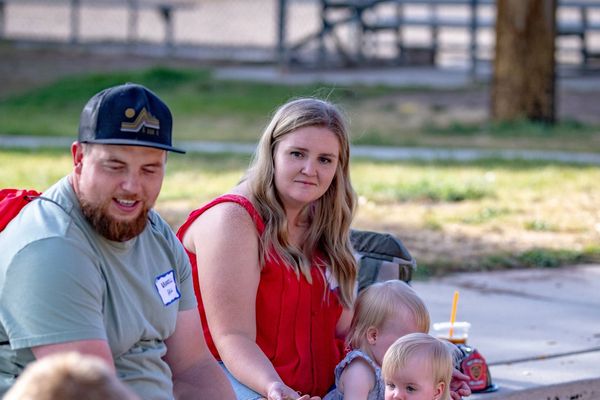 A family with two toddlers sitting on wood chips in a park.